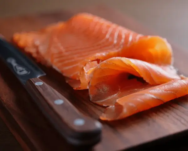 Finísimas lonchas de salmón marinado, listas para disfrutar, junto a un cuchillo de chef sobre tabla de madera.