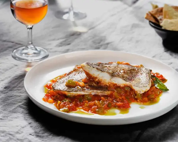 Deliciosa urta a la roteña servida en plato blanco, con vino y pan tostado al fondo.