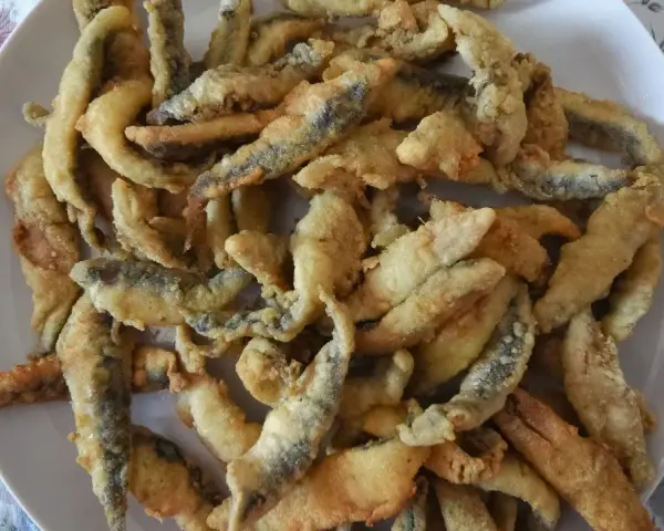 Un plato blanco lleno de boquerones fritos crujientes, listos para disfrutar.