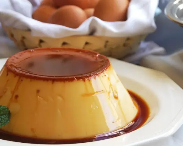 Delicioso flan de huevo casero con caramelo líquido, decorado con menta. En el fondo, una cesta con huevos frescos.