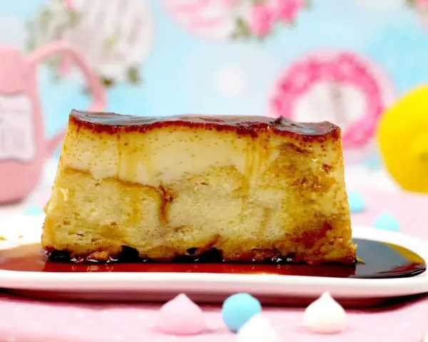Un trozo de pan de calatrava con caramelo líquido, sobre un plato blanco, con merengues de colores y un limón al fondo.