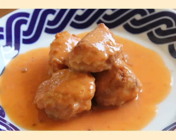 Deliciosas albóndigas de rape en una cremosa salsa naranja, servidas en un plato con borde azul.