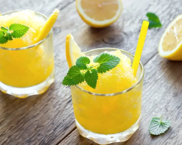 Refrescante granizado de limón, perfecto para un día caluroso. Servido en vasos con rodajas de limón y hojas de menta.
