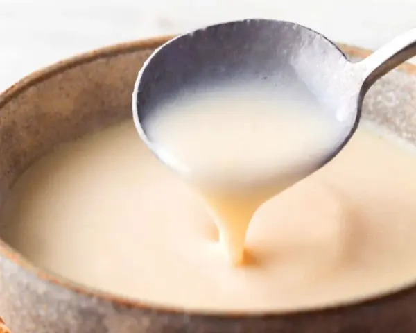 Cuchara sirviendo crema inglesa cremosa en un cuenco rústico.