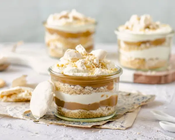 Postres en vaso con capas de bizcocho, crema y dulce de leche, coronados con merengue y polvito canario.