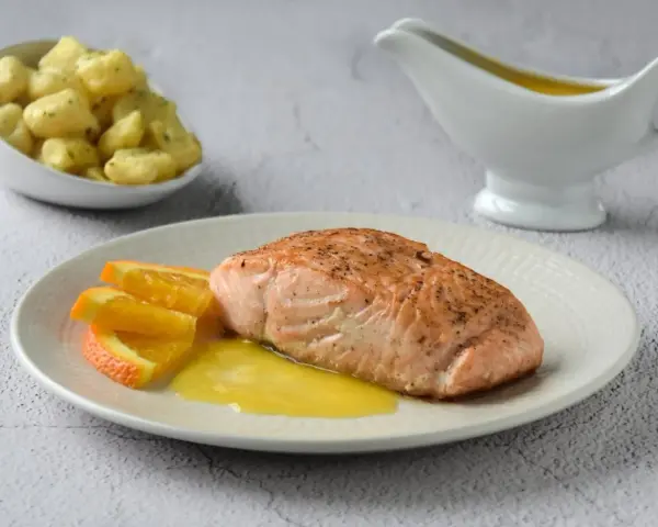 Filete de salmón a la naranja, servido con gajos de naranja y una salsa dorada. Acompañado de gnocchis en un cuenco.