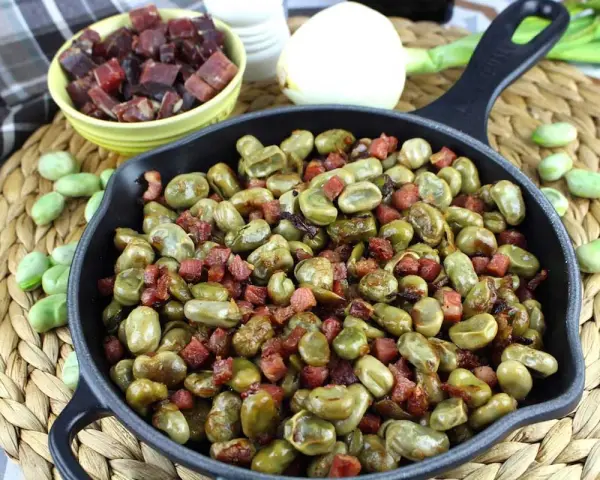 Habas tiernas salteadas con trocitos de jamón en una sartén de hierro fundido, un plato tradicional y delicioso.