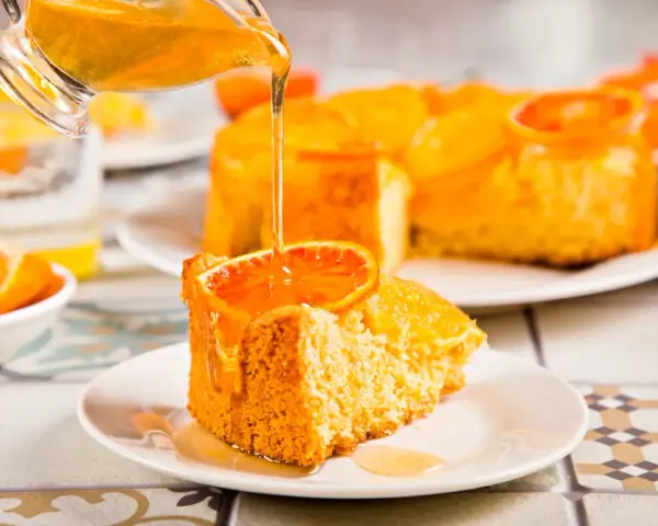 Un trozo de tarta de naranja esponjosa, decorado con una rodaja de naranja y bañado en un almíbar dorado.