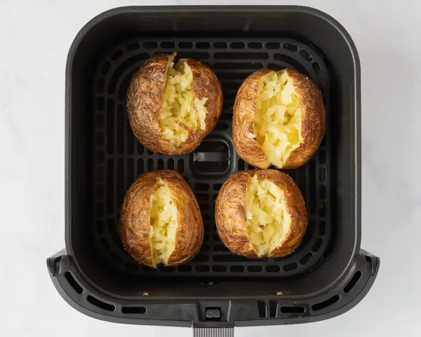 Cuatro patatas asadas en freidora de aire, doradas y crujientes, listas para rellenar.