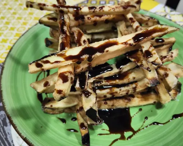 Berenjenas fritas en forma de bastones, bañadas en miel oscura, servidas en un plato verde.