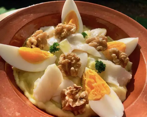 Delicioso plato de atascaburras receta con huevo duro, nueces y perejil en una cazuela de barro.