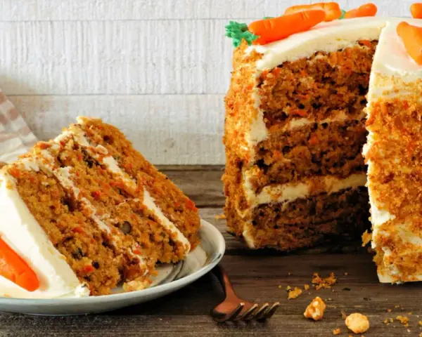 Deliciosa tarta de zanahoria con glaseado cremoso y decoraciones de zanahorias. Una rebanada ya servida en un plato.