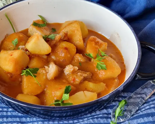 Un reconfortante plato de patatas con bacalao en una salsa rojiza, adornado con perejil fresco.