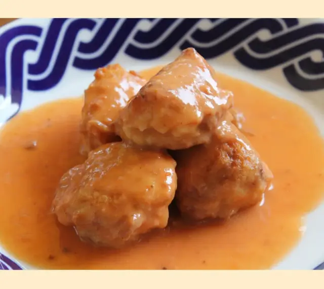 Deliciosas albóndigas de rape en una cremosa salsa naranja, servidas en un plato con borde azul.