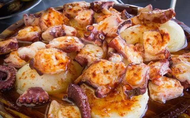 Pulpo a la gallega servido en plato de madera, con patatas cocidas y espolvoreado con pimentón.