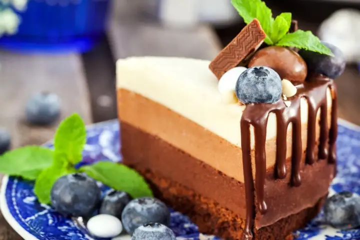 Deliciosa tarta de tres chocolates, con capas de chocolate blanco, con leche y negro, decorada con arándanos y menta.