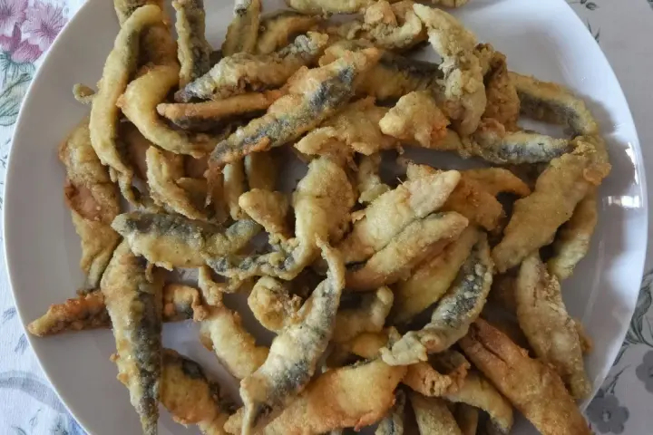 Un plato blanco lleno de boquerones fritos crujientes, listos para disfrutar.