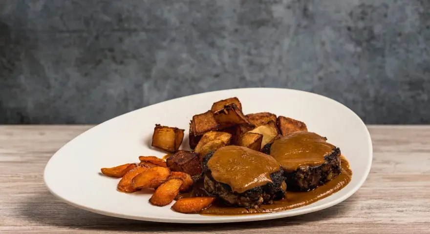 Delicioso plato de cola de toro en salsa, acompañado de patatas rústicas y zanahorias glaseadas.