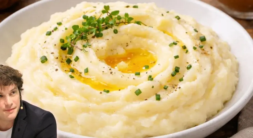 Un hombre sonríe junto a un plato de cremoso puré de patatas, adornado con hierbas frescas y un chorrito de mantequilla derretida.