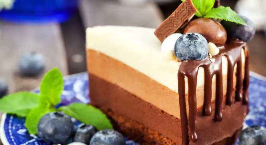 Deliciosa tarta de tres chocolates, con capas de chocolate blanco, con leche y negro, decorada con arándanos y menta.