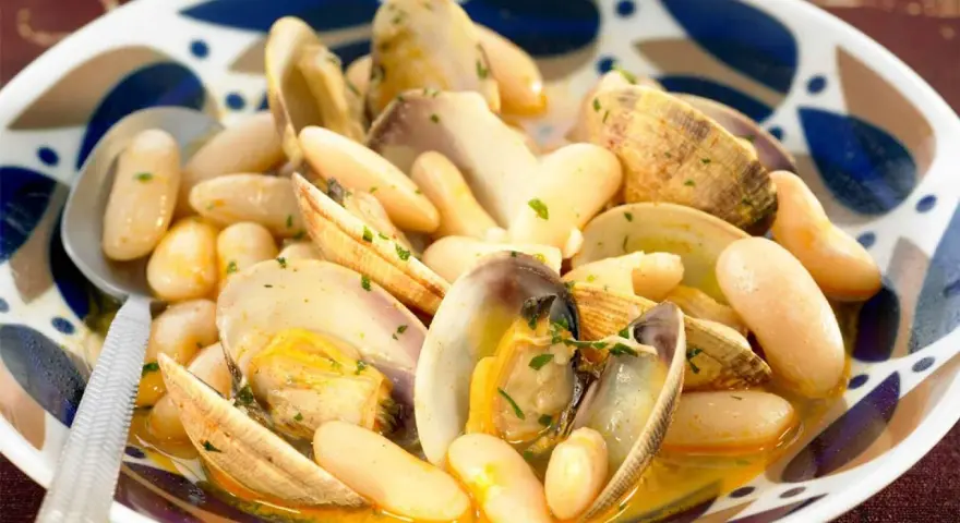 Un plato humeante de fabes con almejas, con judías blancas tiernas y almejas jugosas en una salsa dorada, adornado con perejil picado.