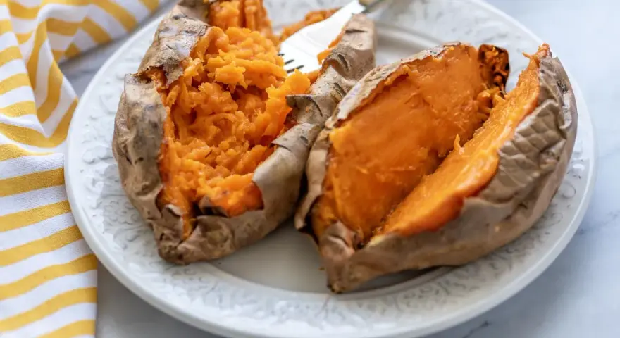 Dos mitades de boniato asado en freidora de aire, servidas en un plato blanco con un tenedor.