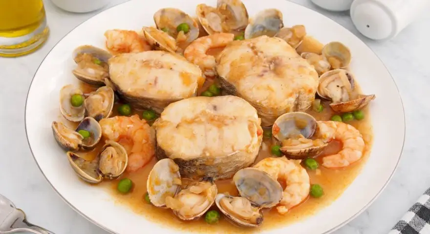 Merluza a la cazuela con gambas, almejas y guisantes en una salsa sabrosa.