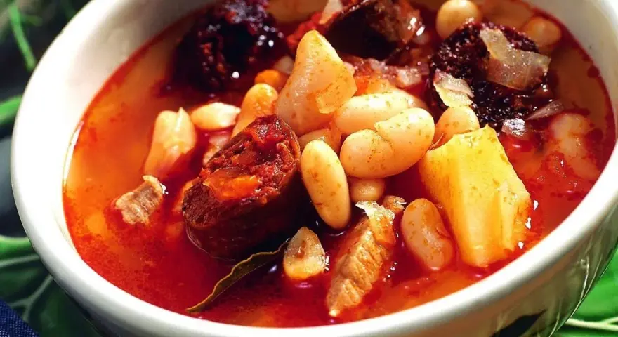Un reconfortante plato de alubias con chorizo, trozos de morcilla y patatas en un cuenco blanco.