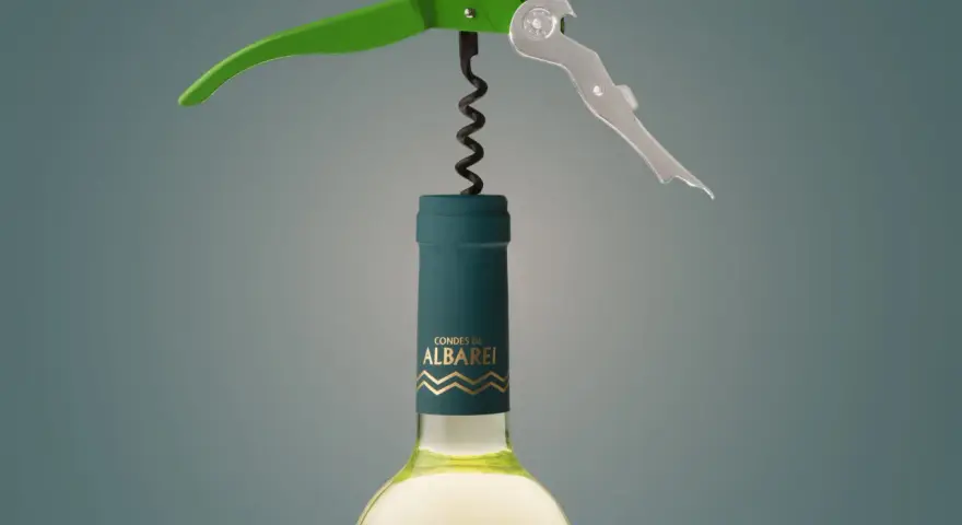 Sacacorchos verde y plateado sobre una botella de vino blanco "Condes de Albarei". El sacacorchos está listo para extraer el corcho, recordándonos de donde viene el corcho.