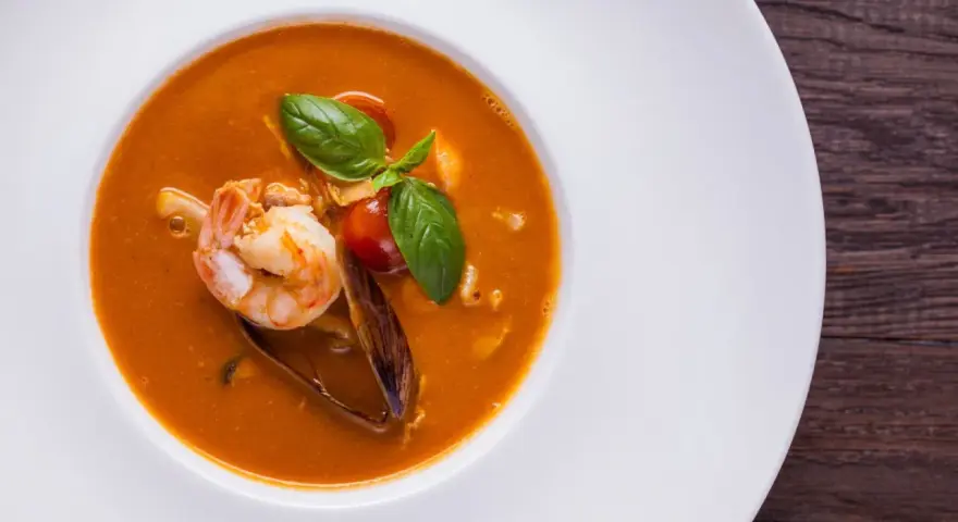 Un plato de zarzuela de pescado con gambas, mejillones y tomate, decorado con albahaca fresca.