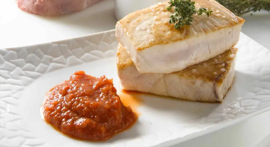 Dos trozos de atún a la plancha apilados, con una cucharada de salsa de tomate y una ramita de tomillo.