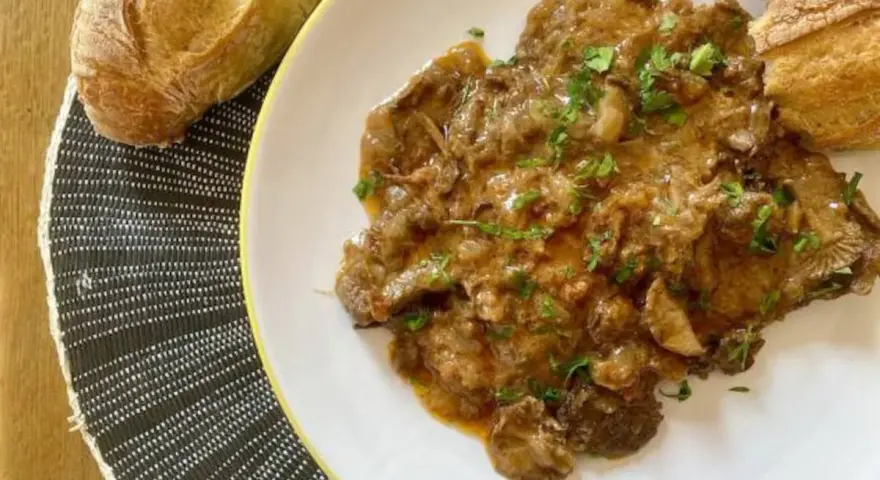 Fricandó, hecho con la parte de la ternera llamada "espalda", servido en plato blanco con pan.