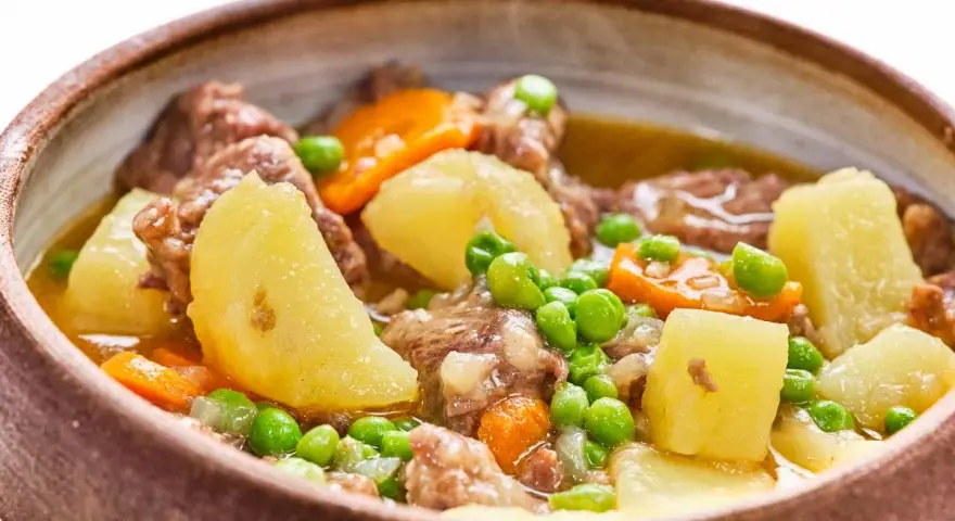 Un reconfortante ragú con trozos de carne tierna, patatas, zanahorias y guisantes en un cuenco rústico.