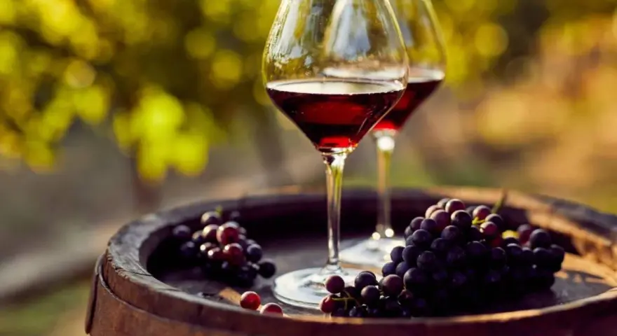 Dos copas de vino tinto y uvas sobre un barril de madera, evocando la esencia de la cosecha Ribera del Duero.