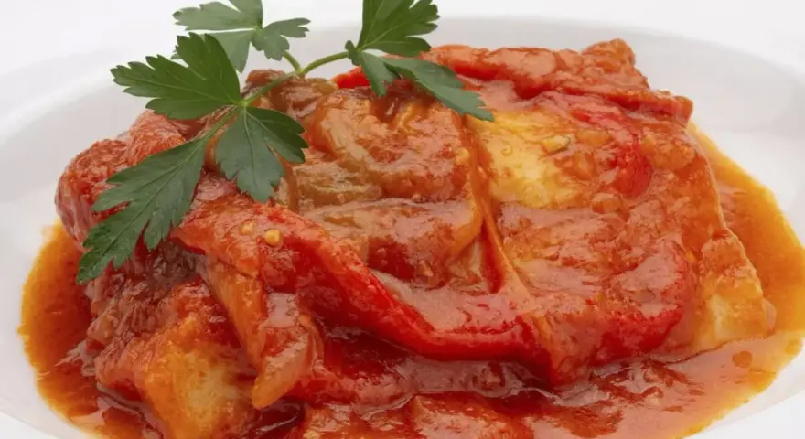 Bacalao a la riojana, un plato tradicional con trozos de pescado blanco cubiertos en una salsa roja de pimientos y tomate, adornado con perejil fresco.