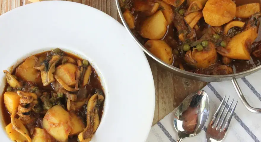 Un plato de papas con choco, un guiso casero con trozos de patata, guisantes y calamares en una rica salsa.