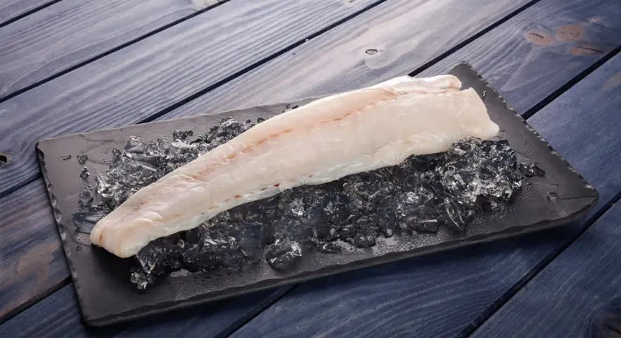 Filete de pescado rosado fresco sobre hielo picado en una tabla negra, listo para cocinar.
