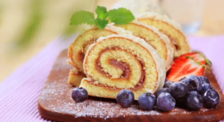 Brazo de gitano en rodajas con fresas y arándanos sobre tabla de madera.