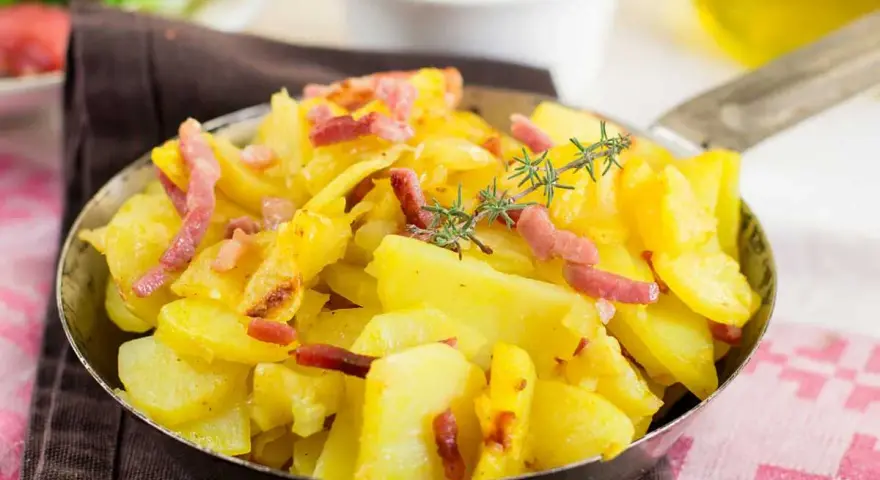 Patatas al microondas con trocitos de bacon crujiente y romero fresco, servidas en una sartén metálica. ¡Un plato sencillo y delicioso!