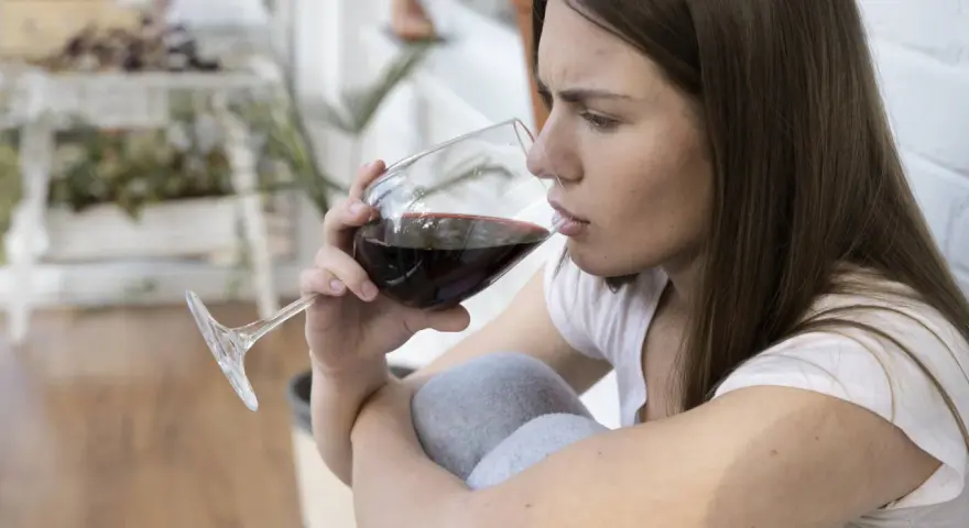 Mujer pensativa bebe vino tinto, recordando que el vino engorda.