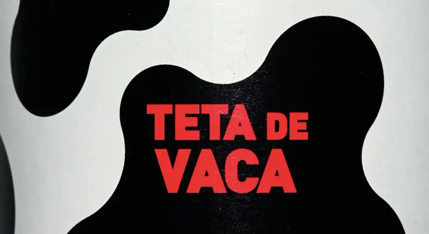Texto rojo "TETA DE VACA" sobre un fondo blanco y negro con manchas de vaca.