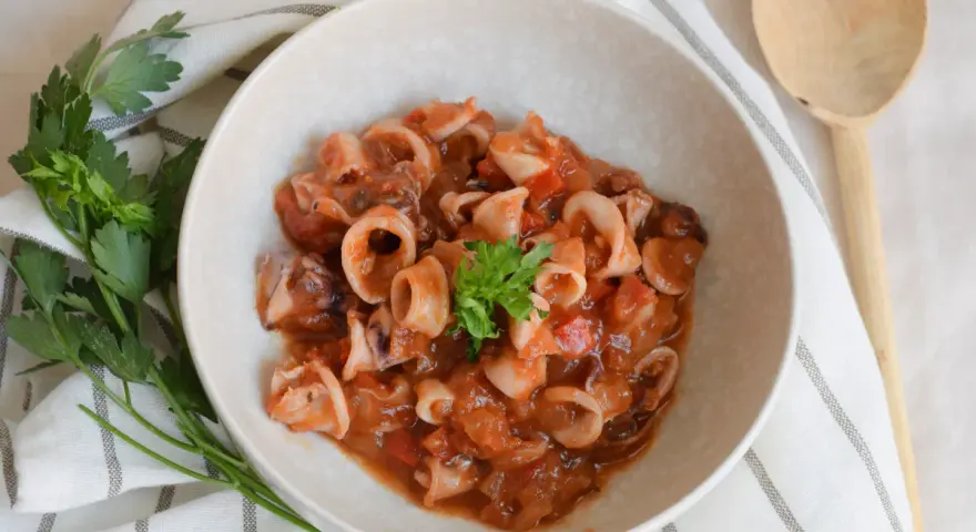 Deliciosos chipirones en salsa de tomate, servidos en un cuenco de cerámica, decorados con perejil fresco.