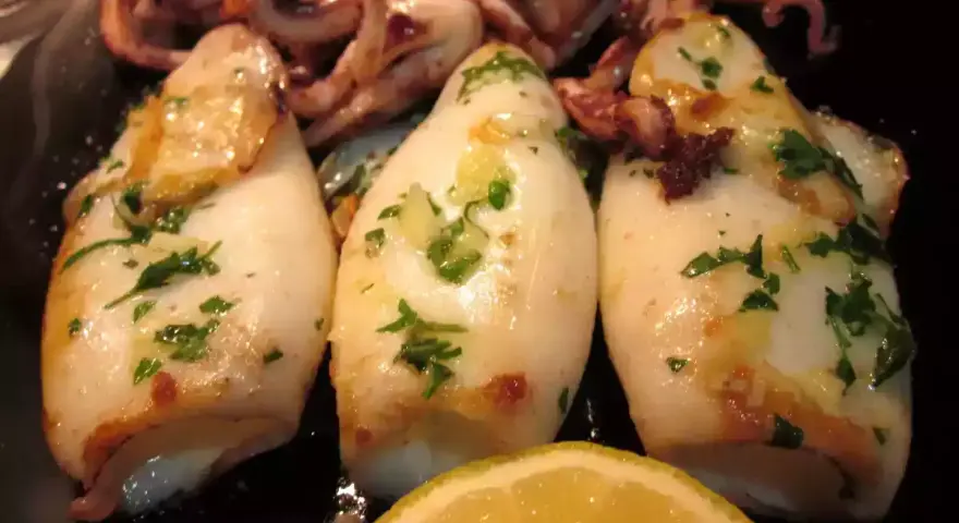 Calamares a la plancha, tiernos y dorados, con perejil fresco y un toque de limón. ¡Un manjar para disfrutar!