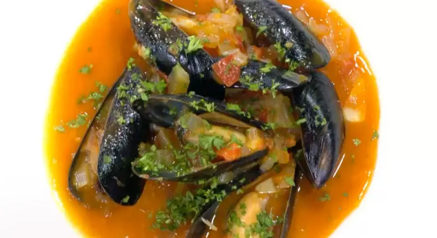 Mejillones a la marinera, jugosos y frescos, nadan en una salsa roja vibrante con perejil picado.