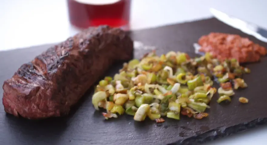 Un jugoso onglet de ternera a la parrilla, acompañado de verduras salteadas y una guarnición rojiza.