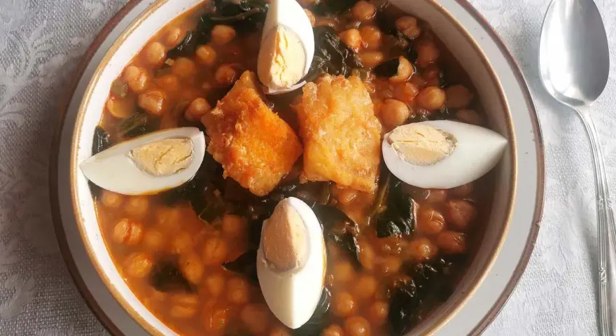 Un reconfortante potaje de vigilia con garbanzos, espinacas, trozos de bacalao rebozado y huevos cocidos, listo para disfrutar.