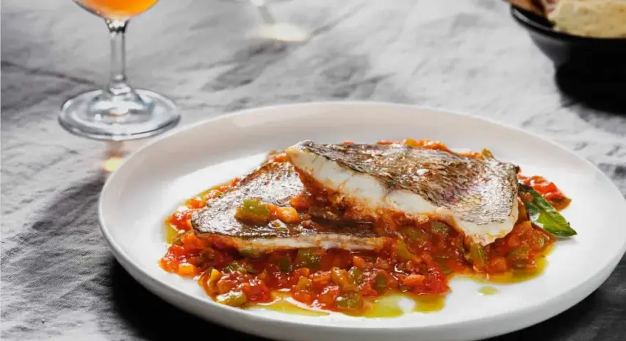 Deliciosa urta a la roteña servida en plato blanco, con vino y pan tostado al fondo.