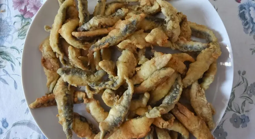 Un plato blanco lleno de boquerones fritos crujientes, listos para disfrutar.