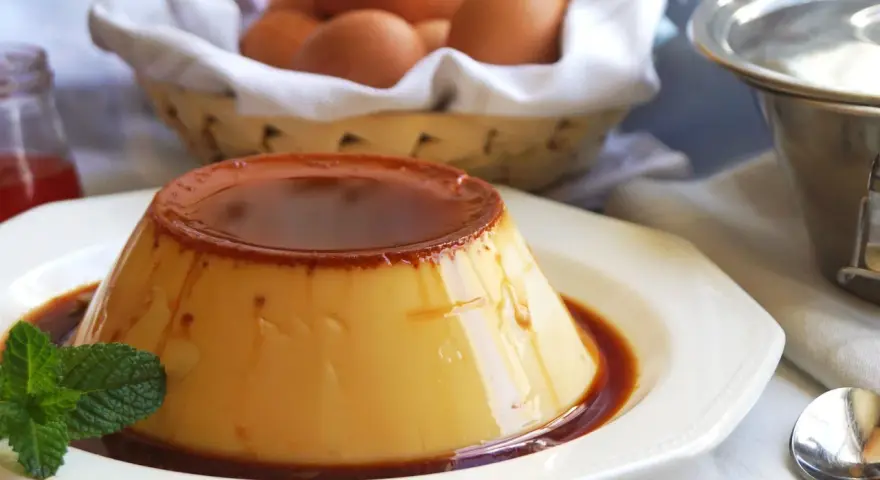 Delicioso flan de huevo casero con caramelo líquido, decorado con menta. En el fondo, una cesta con huevos frescos.
