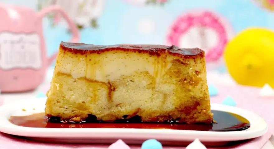Un trozo de pan de calatrava con caramelo líquido, sobre un plato blanco, con merengues de colores y un limón al fondo.